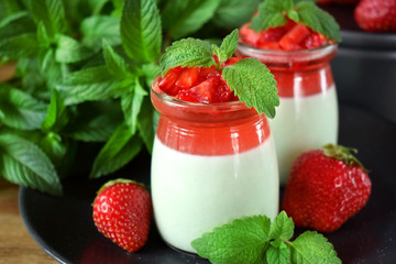 Two layered panna cotta with matcha tea topped with strawberry jelly, berries and mint in glass jars