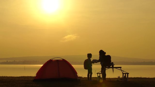 mother and daughter camping by the sea at sunset or sunrise