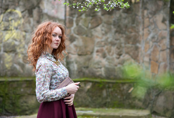 young red-haired curly-haired girl with freckles posing in a summer garden with a vintage book in her hands