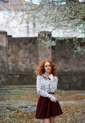 Young red-haired curly girl with freckles posing in autumn in the garden with a vintage book in hands
