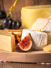 Assorted cheeses on round wooden board plate Camembert cheese, cheese grated bark of oak, hard cheese slices, walnuts, grapes, crackers, bread, thyme, wood background