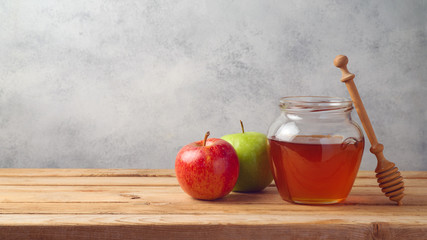 Honey jar and apples on wooden table