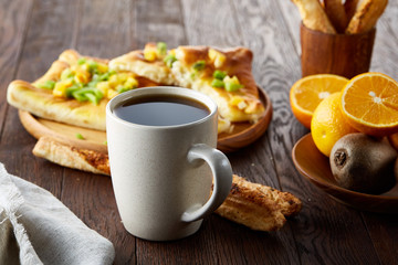 Morning concept with a cup of coffee, breadsticks, fruit pies and oranges on wooden background.
