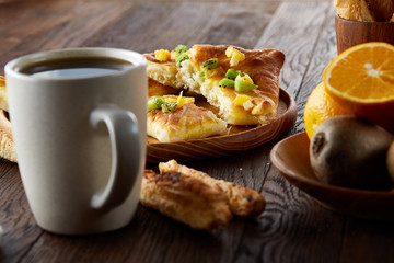 Morning concept with a cup of coffee, breadsticks, fruit pies and oranges on wooden background.