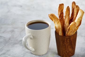 Coffee cup and breadsticks on an grey textured background, close-up, selective focus.