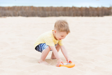 Three years old child plays frisbee on the sand on beach near sea. Beach games and active toddler kid on vacation, happy holiday concept