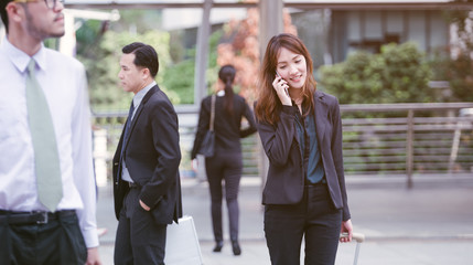 Asian female office worker dressed in stylish formal wear calling on smartphone standing in downtown.