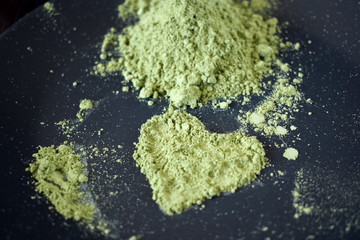 Green matcha tea powder forming a heart on a dark plate