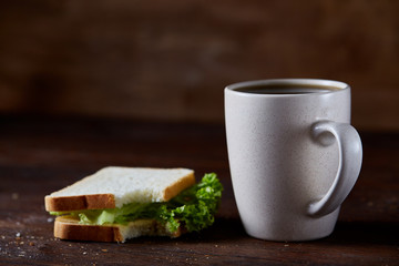 Breakfast table with sandwich and black coffee on rustic wooden background, close-up, selective focus