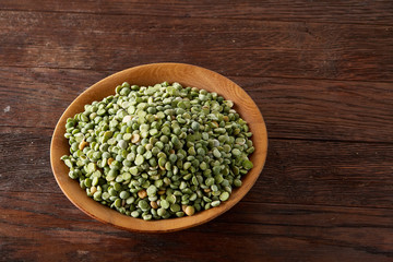 Raw green peas on a wooden plate over rustic background, close-up, selective focus, shallow depth of field.