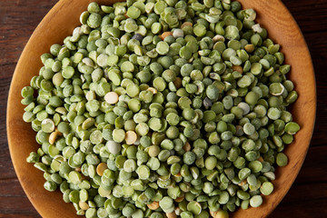 Raw green peas on a wooden plate over rustic background, close-up, selective focus, shallow depth of field.