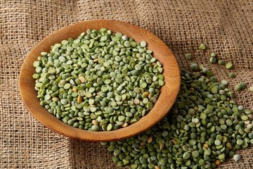 Raw green peas on a wooden plate over burlap tablecloth, close-up, selective focus, top view.