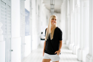 A young and attractive blonde woman standing in an old colonial style building in Asia. She is wearing casual and comfortable clothes as she roams around the new place.