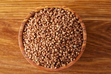 Bowl full of buckwheat grains on rustic wooden table, close-up, selective focus, shallow depth of field.