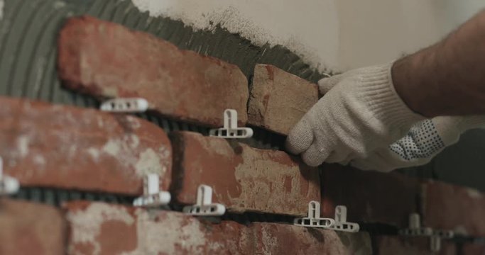 Slow motion closeup worker applying brick cuts tile to the wall