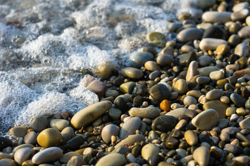 pebble stones on the sea beach, the rolling waves of the sea with foam