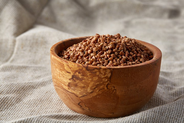 Bowl full of buckwheat grains on rustic wooden table, close-up, selective focus, shallow depth of field.
