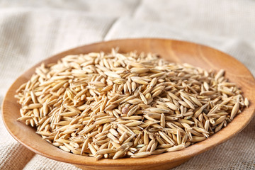 Oat groats or oat spike in wooden plate on homespun tablecloth, copy space, top view, selective focus