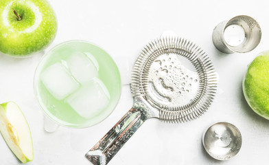 Summer alcoholic cocktail with green apple, vermouth and ice, bar tools, gray background, top view