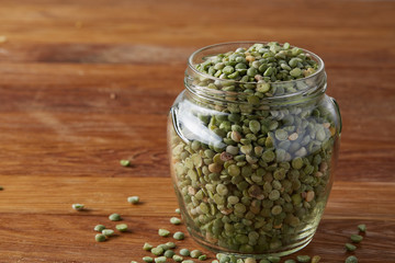 Raw green peas in glass jar over wooden background, close-up, selective focus.