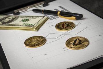 Coins in the form of bitcoin with a bundle of dollars on sheets of statistics