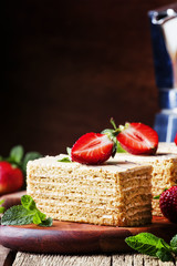 Traditional russian honey cake decorated with strawberries and green mint, old wooden background, selective focus