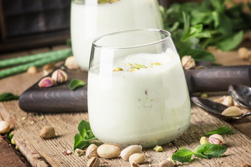 Pistachio milk cocktail with ice cream, nut and green mint, old wooden background, selective focus