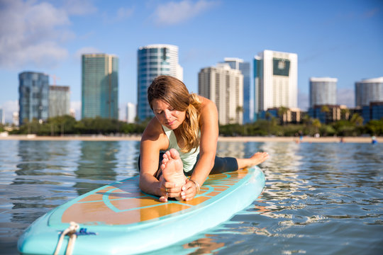 Athletic young woman in SUP Yoga practice front bend Pose in Ala Moana Hawaii