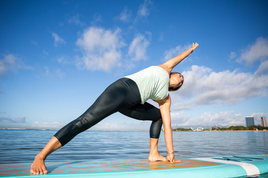 Athletic young woman in SUP Yoga practice side bend Pose in Ala Moana Hawaii