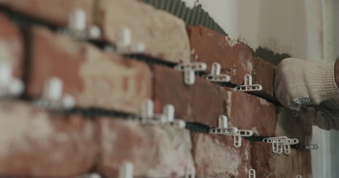 Slow motion closeup worker applying brick cuts tile to the wall