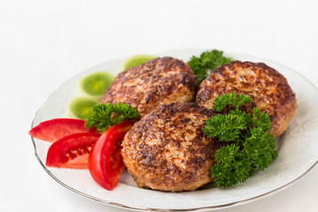 Homemade cutlets with parsley and tomatoes on a white plate and white background.