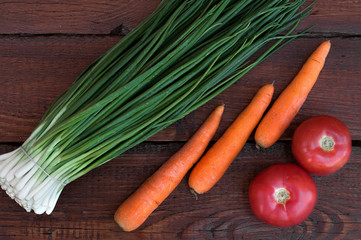 Fresh green onions, washed orange carrots, red ripe tomatoes, beautiful vegetables on a dark wooden table with texture.