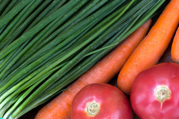 Fresh green onions, washed orange carrots, red ripe tomatoes, beautiful vegetables on a dark wooden table with texture.