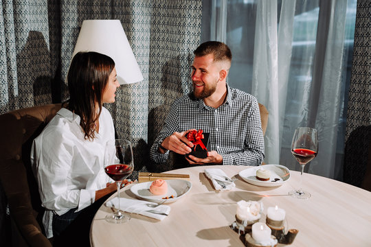 a man opens a gift box on a date.Side view portrait of laughing couple enjoying date in cafe