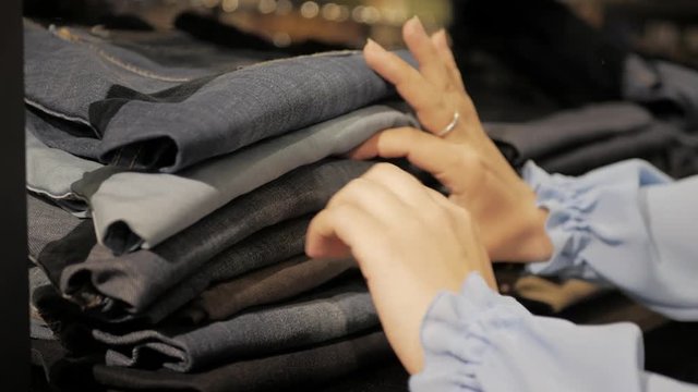 Woman choose new clothes in store , Close-up of hands with denim or jeans on shop shelf