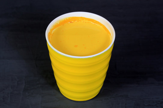 Golden turmeric milk in a yellow cup on a gray