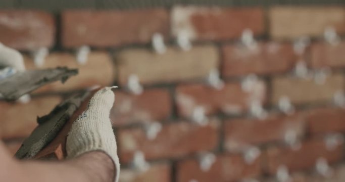 Slow motion closeup worker applying concrete glue to brick tile