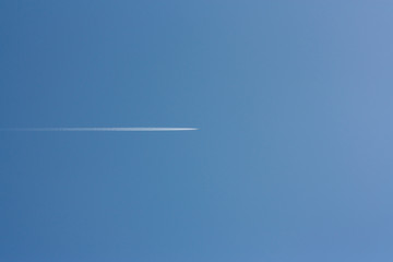 Flying aircraft with an inverse trace against the blue sky