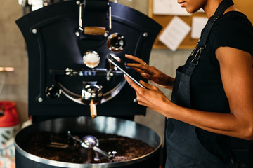 Female barista using digital tablet, standing near coffee roasting machine 