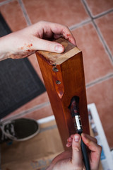 Closeup of hand holding paintbrush and painting wood with brown paint. Hand with brush on the wooden board. Home improvements concept with painting wooden board.