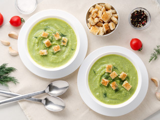 Two large white bowl with vegetable green cream soup of broccoli, zucchini, green peas on white background, top view