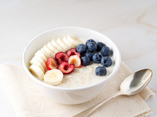 Large bowl of tasty and healthy oatmeal with fruits and berry for Breakfast, morning meal. Side view, white marble table