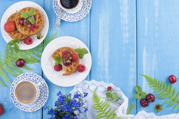 Small pies with berries, strawberries and cherries. Delicious sweet breakfast and fragrant coffee, on a blue wooden background. Above. Flat lay, Copy space,