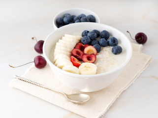 Large bowl of tasty and healthy oatmeal with fruits and berry for Breakfast, morning meal. Side view, white marble table