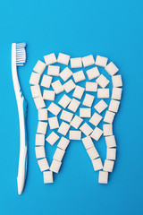 Sugar destroys tooth enamel and leads to tooth decay. Sugar cubes are lined in the form of a tooth on a blue background.