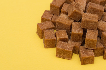 Brown sugar in cubes on a yellow background. An empty place to write a text.