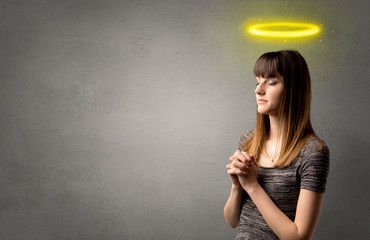 Young woman praying on a grey background with a shiny yellow halo above her head
