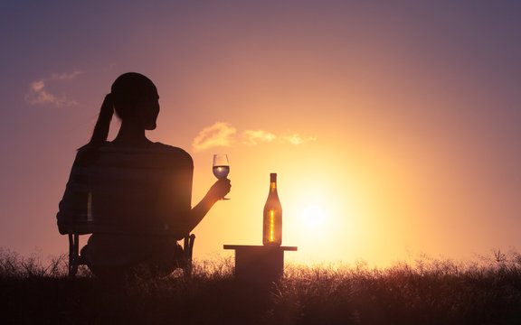 Young woman relaxing outdoors enjoying a glass of wine and a beautiful sunset. 