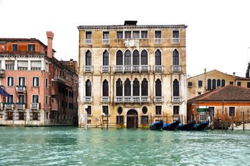 Fototapeta na wymiar Front view of Gothic building facade on The Grand Canal with a row of blue Gondolas, Venice, Italy.