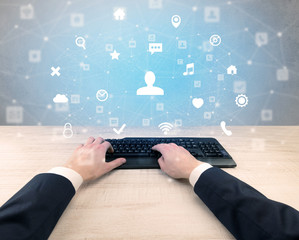 First person view of hand typing with social media concept icons around